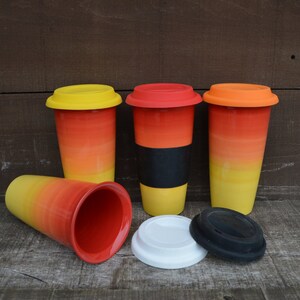 May include: A collection of travel mugs with a gradient design in yellow, orange, and red. The mugs have matching colored lids in yellow, red, and orange. One mug has a black grip. Two lids are white and black.