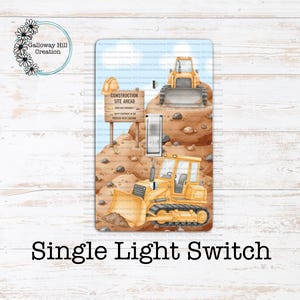 May include: Single light switch cover featuring a construction site design. The cover depicts yellow bulldozers, a construction site sign, and a blue sky background. The text "Construction Site Ahead" is visible.