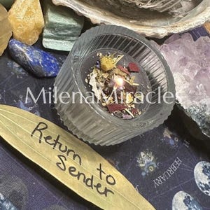 May include: A lit candle in a ribbed glass container, topped with dried herbs and petals. Beside it lies a dried leaf with the handwritten text 'Return to Sender'. The scene includes various crystals and a bundle of white sage in the background.