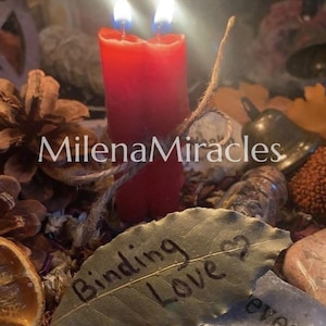 May include: Two red candles joined together with a twine string, positioned behind a dried leaf with the text Binding Love and a heart symbol written on it, surrounded by pinecones, a small metal bell, and various stones.