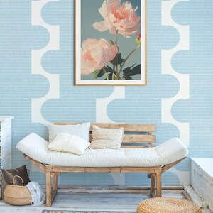 Pu&ograve; includere: Una stampa floreale incorniciata con due grandi peonie rosa chiaro su uno sfondo azzurro. La stampa &egrave; appesa a una parete azzurra con un motivo geometrico bianco. Sotto, un divano in legno con cuscini bianchi.