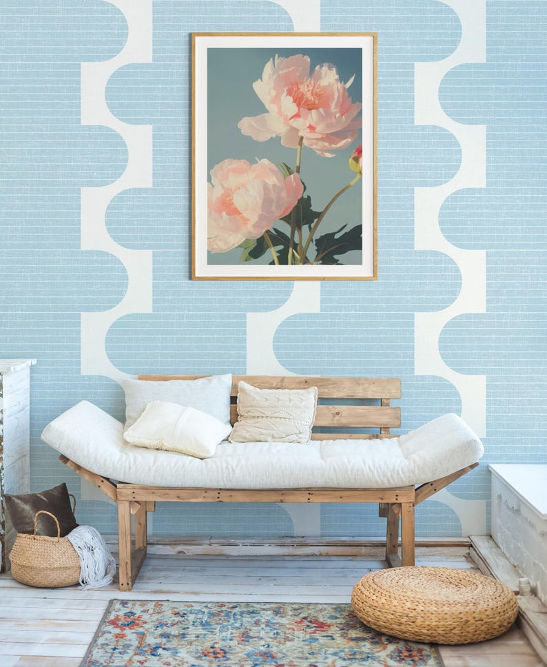 Pu&ograve; includere: Una stampa floreale incorniciata con due grandi peonie rosa chiaro su uno sfondo azzurro. La stampa &egrave; appesa a una parete azzurra con un motivo geometrico bianco. Sotto, un divano in legno con cuscini bianchi.