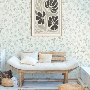 Pu&ograve; includere: Una stampa artistica floreale incorniciata con fiori neri e centri dorati &egrave; appesa a una parete con un motivo floreale verde. Sotto, un divano in legno con cuscini e cuscini bianchi poggia su un tappeto fantasia. Un cesto intrecciato e un pouf completano la scena.