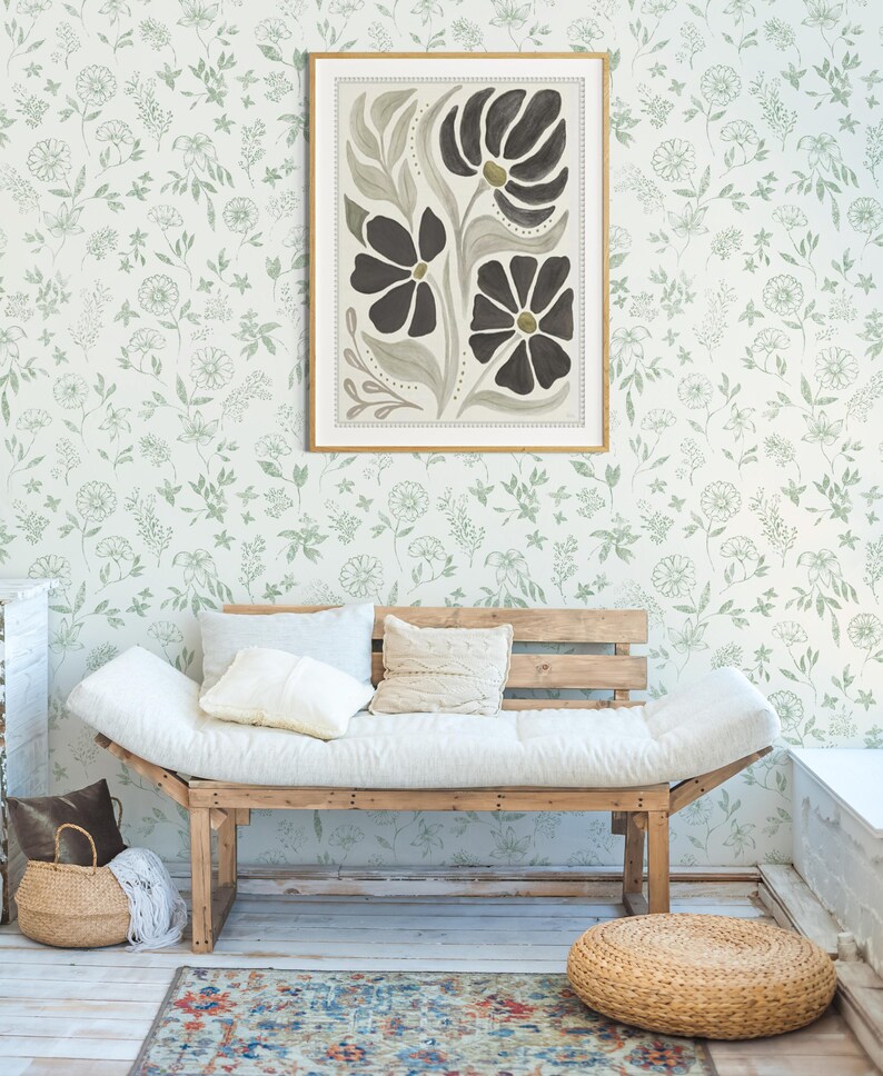 Pu&ograve; includere: Una stampa artistica floreale incorniciata con fiori neri e centri dorati &egrave; appesa a una parete con un motivo floreale verde. Sotto, un divano in legno con cuscini e cuscini bianchi poggia su un tappeto fantasia. Un cesto intrecciato e un pouf completano la scena.