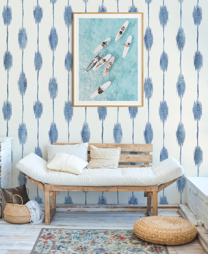 Pu&ograve; includere: Una fotografia incorniciata di surfisti su tavole da surf nell'oceano &egrave; appesa sopra una panca di legno con cuscini e cuscini bianchi. La parete &egrave; decorata con un motivo ikat blu e bianco. Un cesto intrecciato e un tappeto sono sul pavimento.