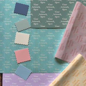 May include: A flat lay of different colored wrapping paper with a repeating pattern of the text "Your Artwork Here". The wrapping paper is in shades of blue, pink, beige, and yellow.