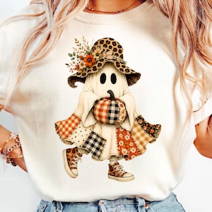 Könnte beinhalten: Ein cremefarbenes T-Shirt mit einer Grafik eines Geistes, der einen Hut mit Leopardenmuster trägt, welcher mit orangefarbenen und weißen Blumen verziert ist. Der Geist hält einen karierten Kürbis und trägt Patchwork-Kleidung mit Vichy-Muster und Leoparden-Sneakern.