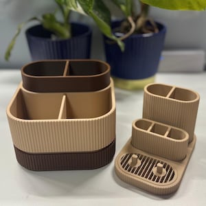 May include: A collection of beige and brown desk tidies. The set includes a stackable organiser with two compartments, a smaller organiser with three compartments, and a tray with two cylindrical holders.