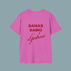 Puede incluir: Una camiseta de color rosa brillante de manga corta con texto rojo oscuro impreso en la parte delantera. El texto dice DANAS SAMO en una fuente negrita sin remates, seguido de la palabra Ljubav escrita en una fuente cursiva debajo.