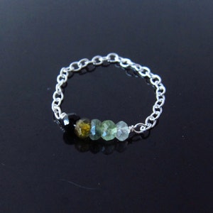 以下が含まれることがあります： 黒、緑、黄色の宝石が並んだシルバーチェーンリングです。