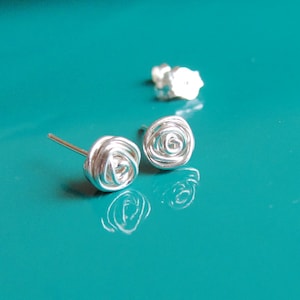 Può includere: Un paio di orecchini a lobo in argento a forma di rosa. Gli orecchini sono realizzati in filo attorcigliato a forma di rosa.