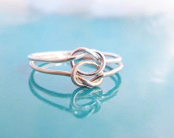 May include: A silver knot ring with a double band. The ring is made of two intertwined bands of silver, creating a knot shape.