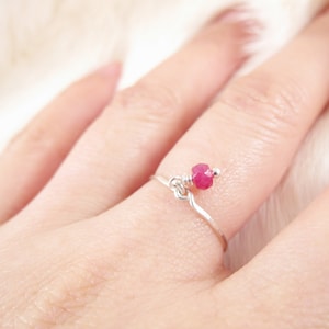 May include: A delicate silver ring with a single pink gemstone dangling from the band.