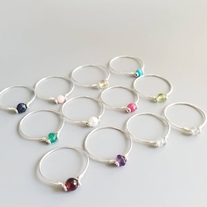May include: A set of 10 silver rings with different colored gemstones. The rings are simple and delicate, with a single gemstone wrapped in wire.