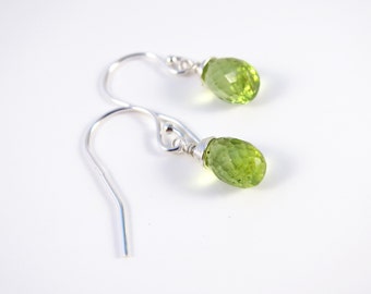 Peut inclure: Une paire de boucles d'oreilles en argent avec des gouttes de pierres précieuses vertes. Les boucles d'oreilles sont faites de fil enroulé autour des pierres.