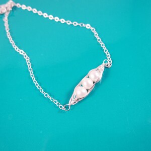 May include: A silver chain necklace with a silver pea pod charm featuring three white pearls.