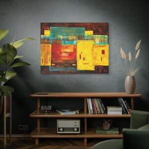 May include: Abstract painting with geometric shapes in shades of yellow, red, blue, and green. The painting is framed and hanging on a dark gray wall.