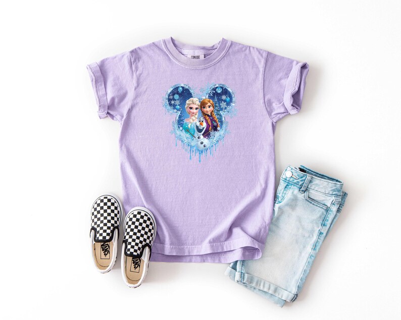May include: A lilac t-shirt with a Frozen graphic of Elsa and Anna in a Mickey Mouse shape. The outfit includes light blue denim shorts and black and white chequered slip-on shoes.