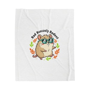 Puede incluir: Manta blanca con una ilustración de dibujos animados de un roedor marrón con gafas de sol. El texto "Rad Rascally Rodent" está encima del roedor en un diseño circular. El roedor está rodeado por una corona de hojas verdes y naranjas.
