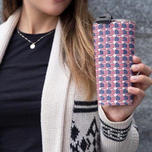 Pode incluir: Um copo de aço inoxidável com um padrão repetido da bandeira americana. O design apresenta listras vermelhas e brancas com campos azuis de estrelas brancas. O copo tem uma tampa preta.