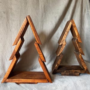 May include: Two wooden tree-shaped shelves. The shelves are made of stained wood in varying shades of brown. Each shelf has a triangular shape with horizontal shelves. The shelves are designed to resemble stylized Christmas trees.