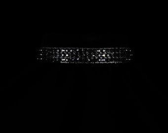 May include: A black choker necklace with multiple rows of small, sparkling embellishments. The choker is set against a dark background, highlighting the reflective quality of the adornments. The design suggests a formal or evening wear accessory.