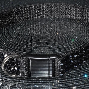 K&ouml;nnte beinhalten: Ein schwarzes Haustierhalsband mit einem funkelnden, edelsteinartigen Design. Das Halsband verf&uuml;gt &uuml;ber eine robuste Schnalle und einen Metall-D-Ring zur Befestigung der Leine. Das Halsband besteht aus einem strapazierf&auml;higen, gewebten Material.