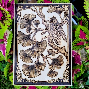 May include: A rectangular wooden plaque featuring a pyrography design of a cicada perched on a ginkgo branch. The artwork is enclosed within a decorative border, showcasing detailed line work of the insect and fan-shaped ginkgo leaves.