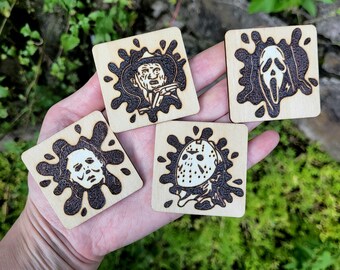 May include: Four square wooden coasters with horror movie character designs. Each coaster features a different character, including Freddy Krueger, Ghostface, Michael Myers, and Jason Voorhees, in a dark brown splatter design.