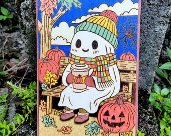 May include: Wooden art piece featuring a friendly ghost wearing a hat and scarf, holding a coffee cup, and sitting on a bench with pumpkins. The background includes a tree, leaves, and a spiderweb. The color palette includes orange, yellow, green, and blue.