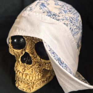 May include: A white cotton skullcap with a blue and white floral pattern. The skullcap is folded over and has a white brim.