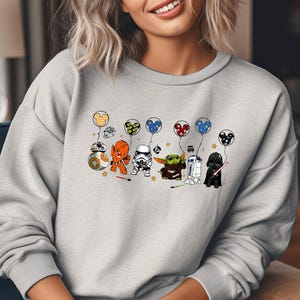 May include: A gray sweatshirt with a print of Star Wars characters holding balloons with Mickey Mouse ears. The characters include Chewbacca, R2-D2, Darth Vader, Yoda, and a Stormtrooper.