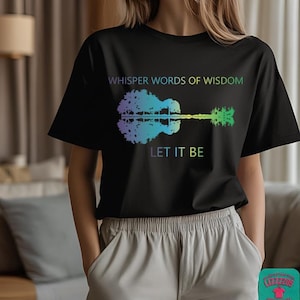 May include: A black short-sleeved t-shirt featuring a colorful gradient graphic of a guitar shaped like a tree with its reflection. The text reads WHISPER WORDS OF WISDOM above the guitar and LET IT BE below the guitar in a multi-colored font.