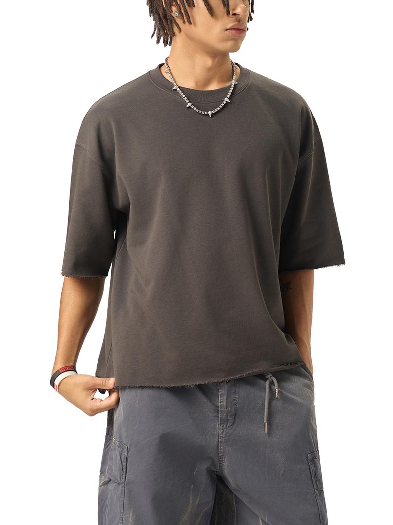 A dark gray, half-sleeved t-shirt with a raw hem and relaxed fit. The shirt is paired with gray cargo shorts. A silver necklace with spike accents is visible.