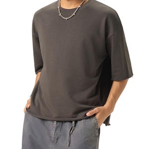 A dark gray, half-sleeved t-shirt with a raw hem and a crew neck. The shirt is paired with gray cargo pants with a drawstring. A silver necklace with spike-like accents is worn.