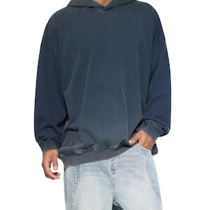 Puede incluir: Una sudadera con capucha azul oscuro con un aspecto descolorido. La sudadera con capucha tiene una capucha con cordón, mangas largas y un bolsillo de canguro. El modelo lleva vaqueros azules claros.