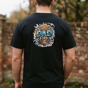 Könnte beinhalten: Schwarzes T-Shirt mit dem farbenfrohen Schriftzug "Best Dad Ever". Das Design beinhaltet Werkzeuge wie Schraubenschlüssel und einen Hammer, mit Farbspritzern in Blau, Gelb und Orange.