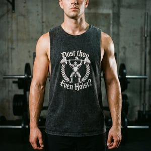 May include: A dark grey sleeveless vest with the white text "Dost thou even hoist?" and a weightlifter graphic. The design is encircled by a laurel wreath. The vest has a faded, vintage appearance, suitable for gym wear.
