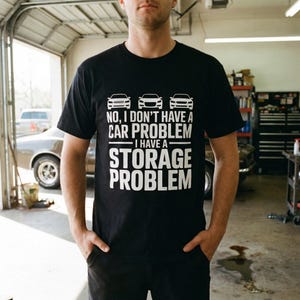 Puede incluir: Camiseta negra con texto blanco y gráficos de coches. El texto dice: "NO, NO TENGO UN PROBLEMA CON EL COCHE, TENGO UN PROBLEMA DE ALMACENAMIENTO". La camiseta presenta tres siluetas de coches encima del texto.