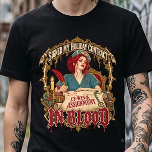 May include: A black t-shirt featuring a graphic of a red-haired nurse in a teal uniform writing with a red quill on a scroll. The text reads SIGNED MY HOLIDAY CONTRACT, 13-WEEK ASSIGNMENT, and IN BLOOD, surrounded by a gold ornate bone frame.