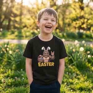 May include: A black t-shirt with a graphic of a muscular Easter bunny holding a basket of eggs and wearing sunglasses. The word "EASTER" is printed in yellow below the graphic. The shirt is worn by a smiling child.