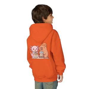 kid wearing orange Youth hoodie white with cute axolotl and capybara design