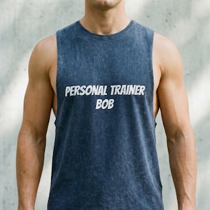 May include: A sleeveless, dark blue tank top with the text "PERSONAL TRAINER BOB" in white. The shirt has a slightly faded appearance and a rounded neckline. The image shows the upper torso of a person wearing the shirt.