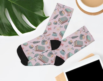 May include: A pair of lavender socks with a pattern of books, teacups, bows, and glasses. The socks have black heels and toes. The design includes teal, pink, and white elements. The socks are likely made of a soft, comfortable material.