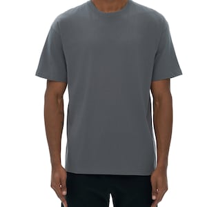 Puede incluir: Una camiseta gris carbón con cuello redondo y mangas cortas. La camiseta está hecha de un material suave y se combina con pantalones cortos negros. El modelo está de pie frente a un fondo blanco.