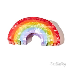 May include: A rainbow-coloured hair clip made of plastic. The clip is shaped like a rainbow with seven colours: red, orange, yellow, green, blue, indigo, and violet. The clip is designed to hold hair in place.