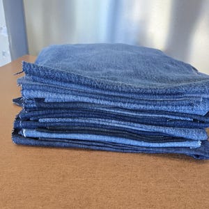 Może przedstawiać: Stos tkaniny dżinsowej w różnych odcieniach niebieskiego, od jasnego do ciemnego.
