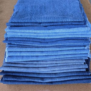 Könnte beinhalten: Ein Stapel Denim-Stoffstücke in verschiedenen Blautönen, von hell bis dunkel. Die Stoffstücke sind rechteckig geschnitten und haben sichtbare rohe Kanten. Die Anordnung deutet auf eine Sammlung von Materialien für Näh- oder Bastelprojekte hin.