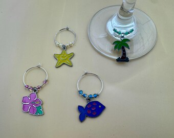 Könnte beinhalten: Satz mit vier bunten Glasanhängern mit verschiedenen Designs: einer rosa Hibiskusblüte, einem blauen Fisch, einem gelben Seestern und einer grünen Palme. Die Anhänger sind an silbernen Ringen mit Perlen befestigt.