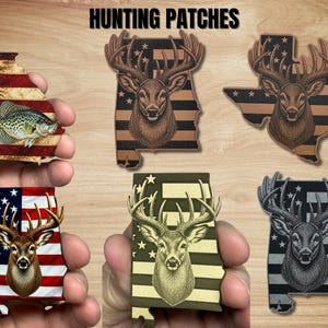May include: A collection of six state-shaped patches featuring hunting themes. Designs include a fish on a Georgia-shaped flag patch and five deer head illustrations overlaid on various state-shaped American flag patterns in different color schemes.